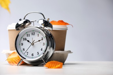 Photo of Alarm clock, dry leaves and cups of coffee on light grey background, closeup. Space for text