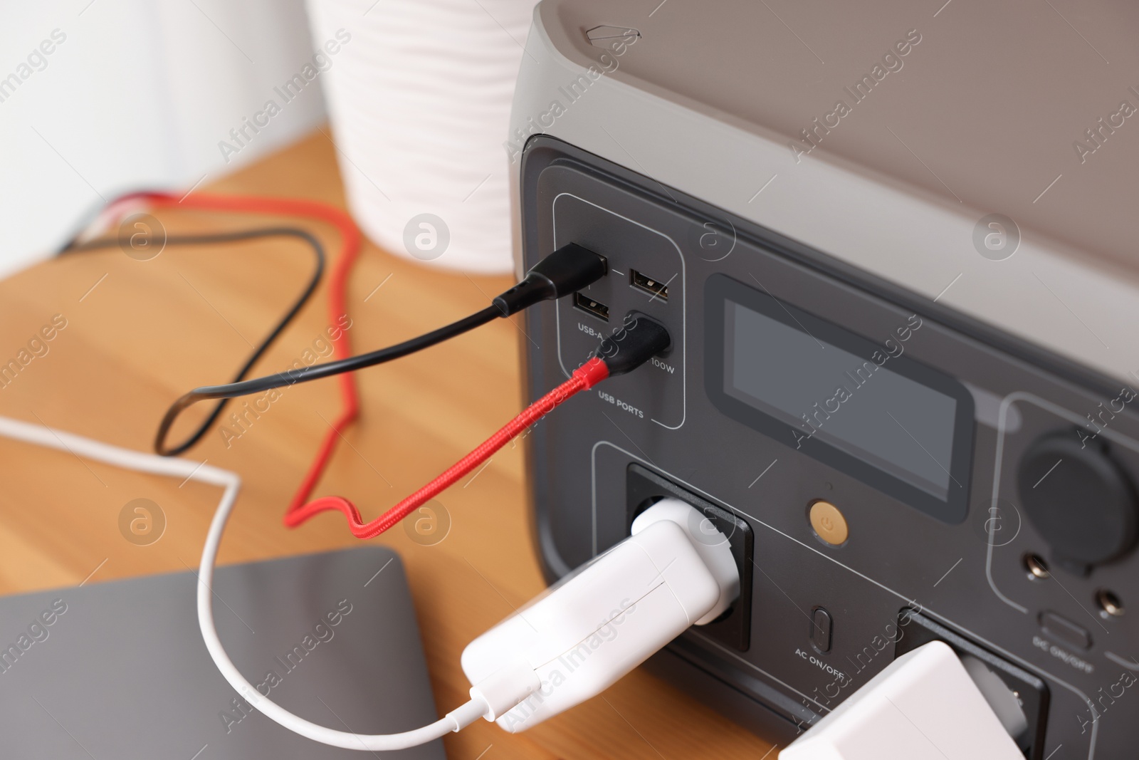 Photo of Portable power station with chargers on wooden desk indoors, closeup