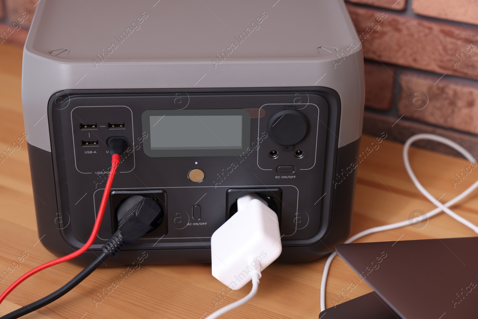 Photo of Laptop charging from portable power station on wooden desk indoors