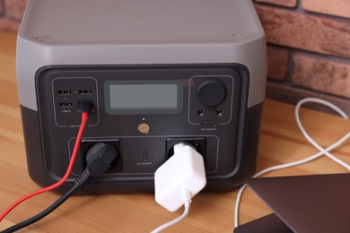 Photo of Laptop charging from portable power station on wooden desk indoors