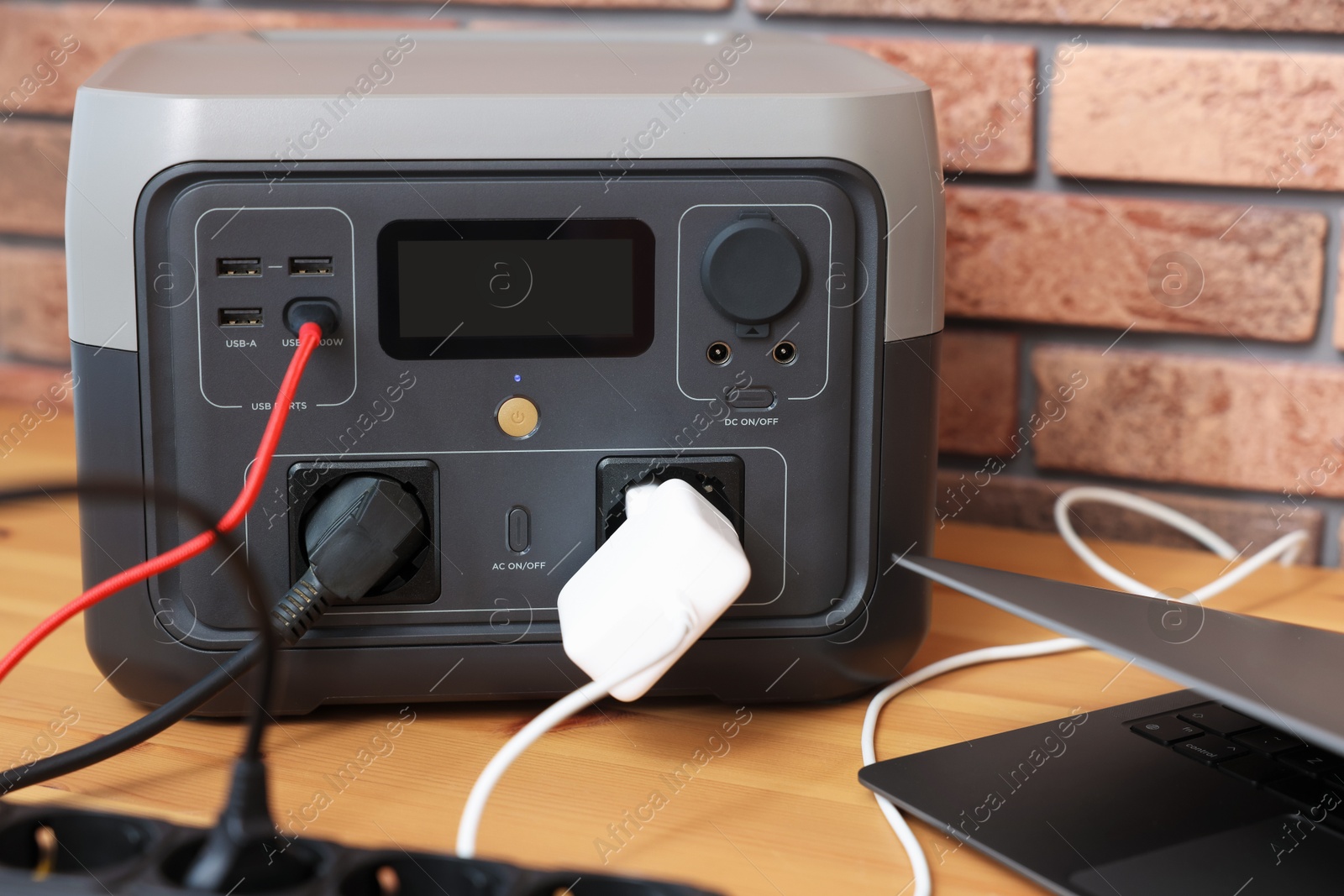 Photo of Laptop charging from portable power station on wooden desk indoors