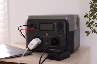 Photo of Laptop charging from portable power station on wooden table indoors