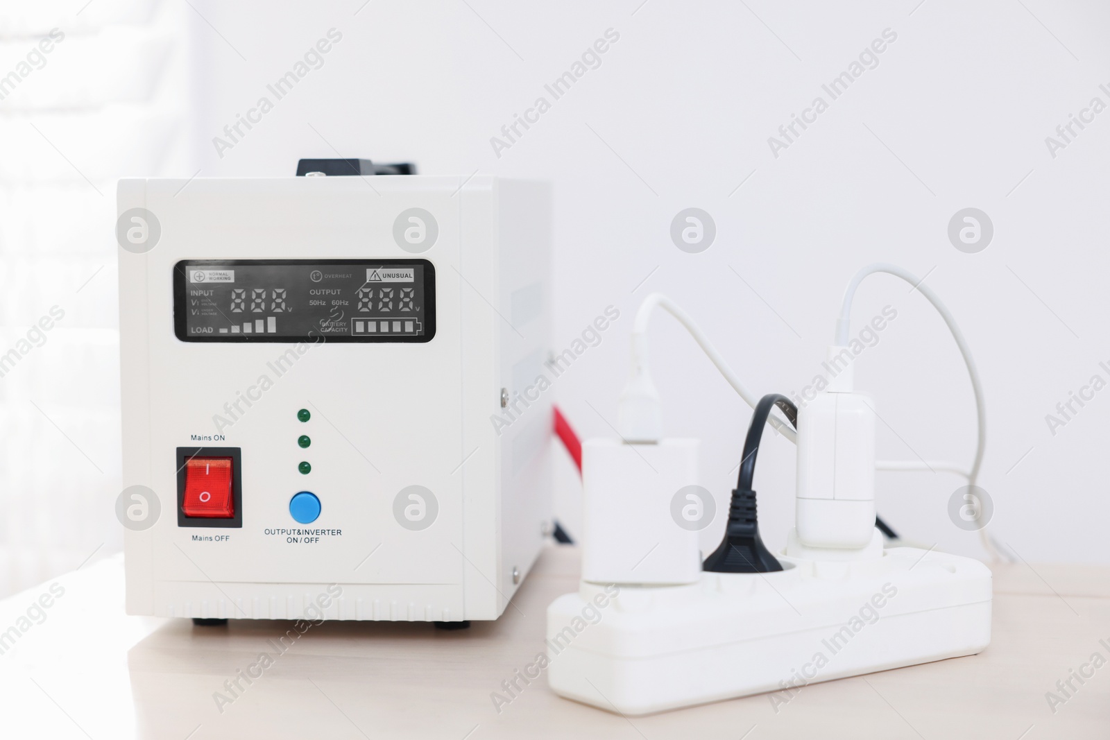 Photo of Portable power station and multi-socket extension board with chargers on table indoors