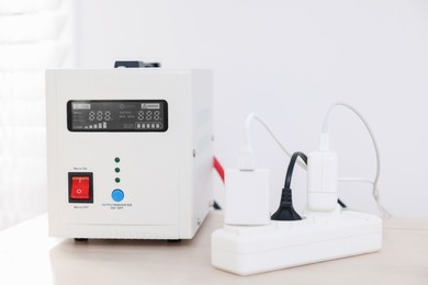 Photo of Portable power station and multi-socket extension board with chargers on table indoors