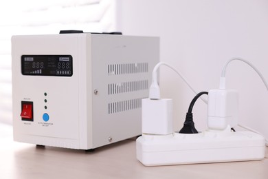 Photo of Portable power station and multi-socket extension board with chargers on table indoors