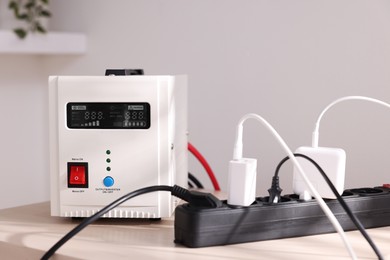 Photo of Portable power station and multi-socket extension board with chargers on table indoors