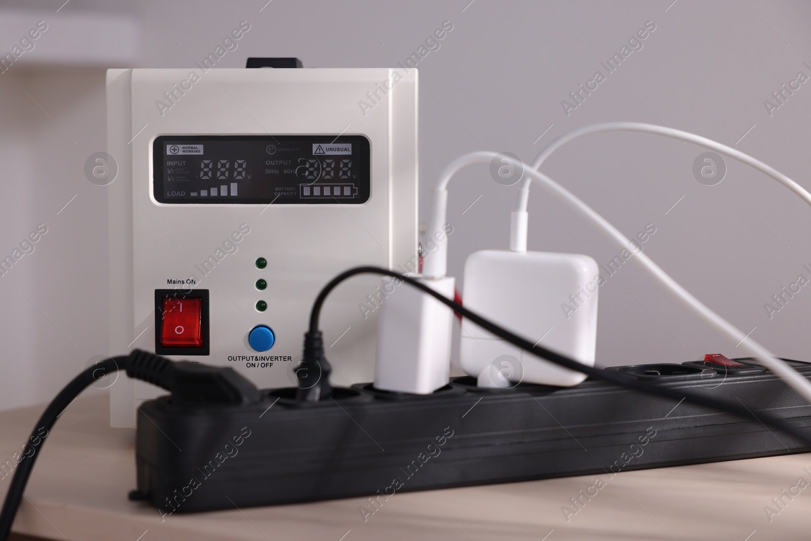 Photo of Portable power station and multi-socket extension board with chargers on table indoors