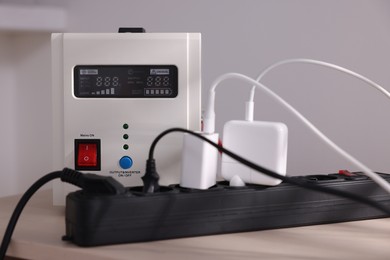 Photo of Portable power station and multi-socket extension board with chargers on table indoors