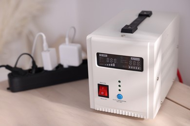 Photo of Portable power station and multi-socket extension board with chargers on table indoors, closeup