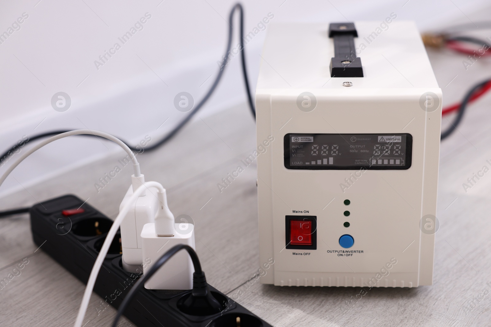 Photo of Portable power station and multi-socket extension board with chargers on table indoors