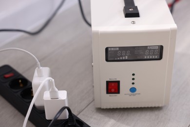 Photo of Portable power station and multi-socket extension board with chargers on table indoors, closeup