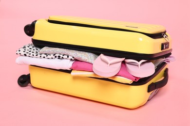 Packed suitcase full of clothes on pink background, closeup