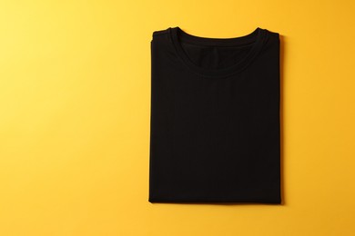 Photo of Blank black t-shirt on yellow background, top view. Mockup for design