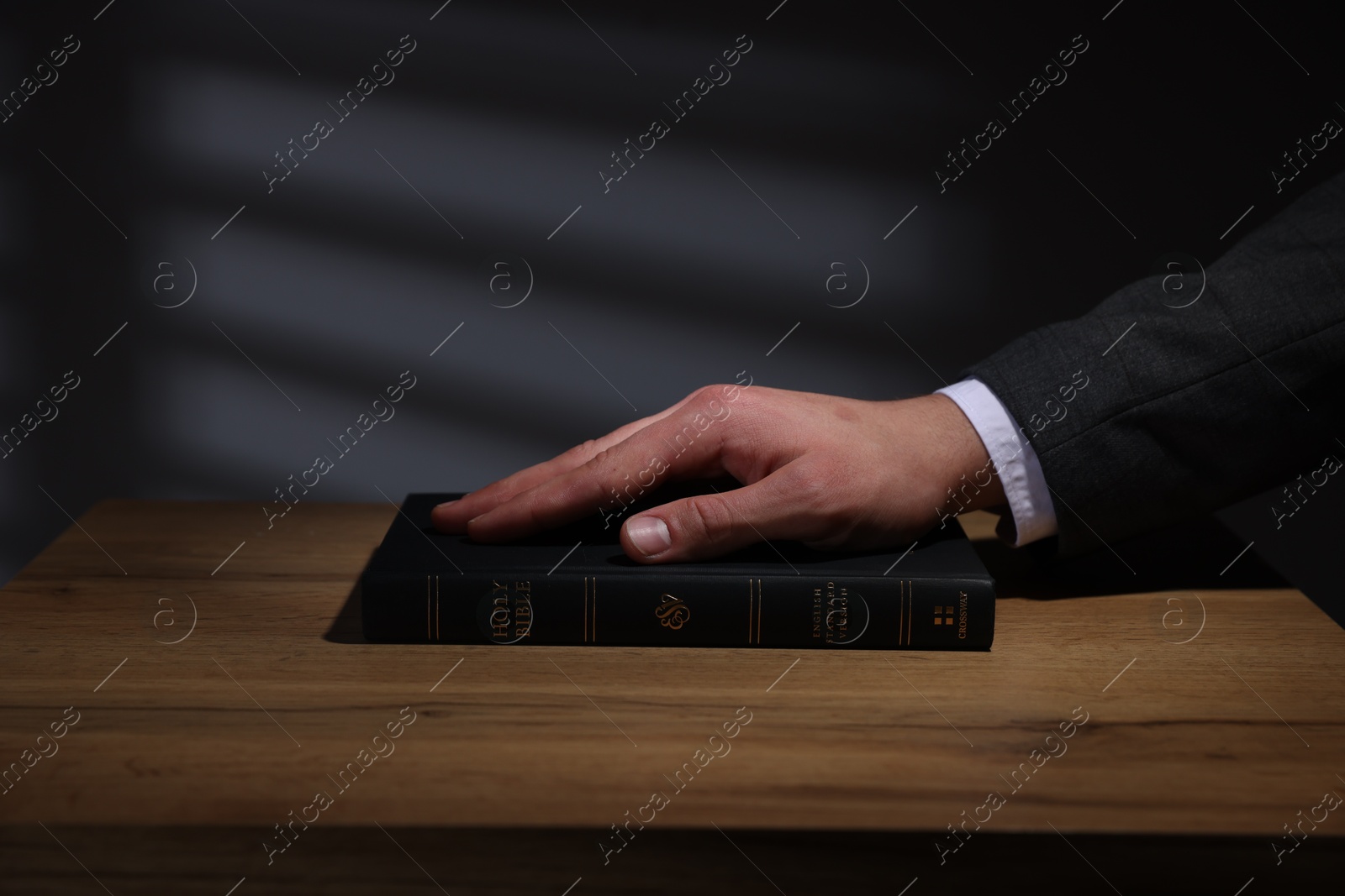 Photo of Man taking oath with his hand on Bible at wooden table, closeup