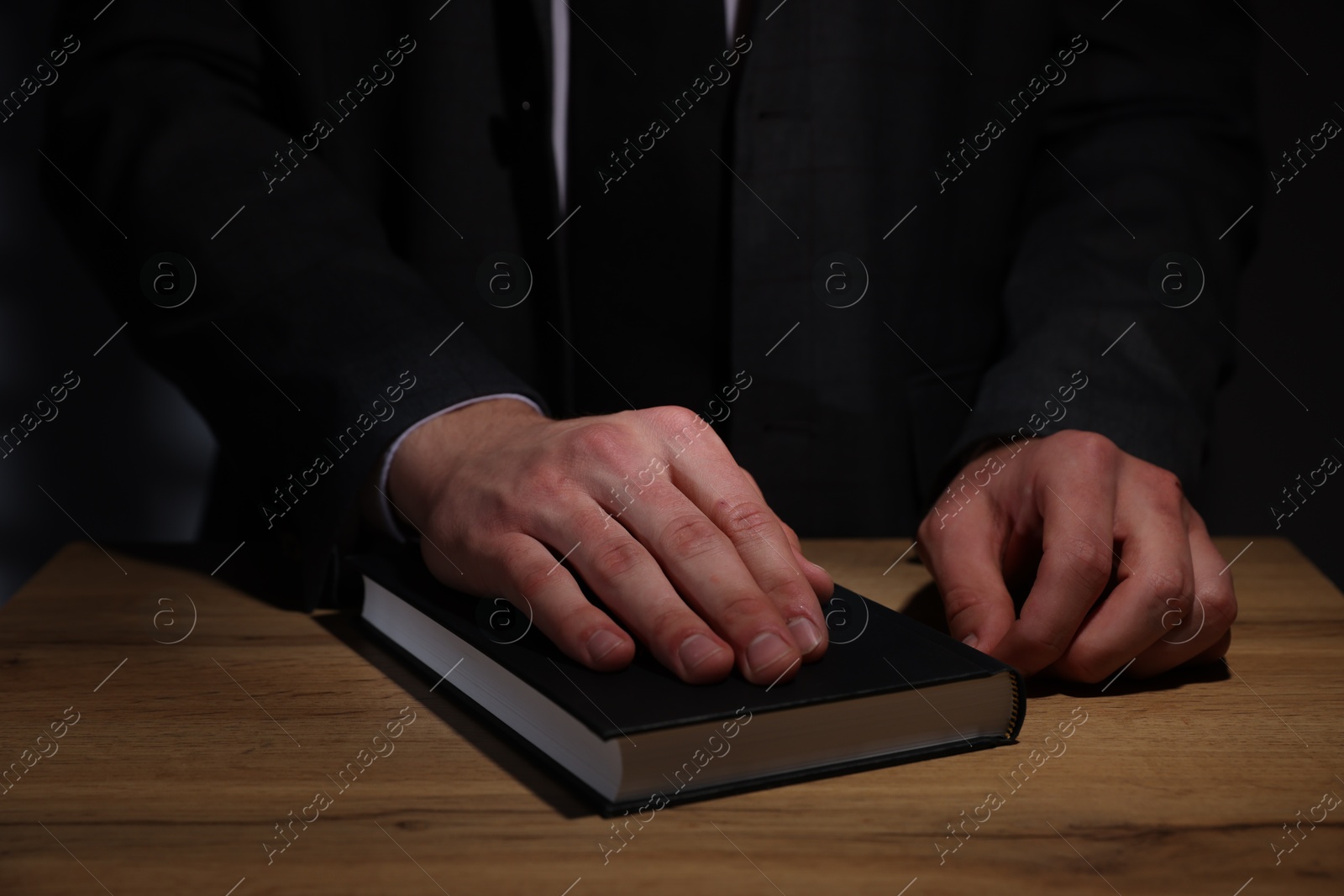 Photo of Man taking oath with his hand on Bible at wooden table, closeup