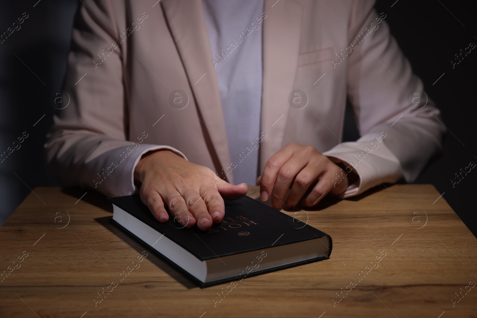 Photo of Woman taking oath with her hand on Bible at wooden table, closeup