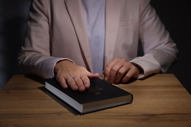 Photo of Woman taking oath with her hand on Bible at wooden table, closeup