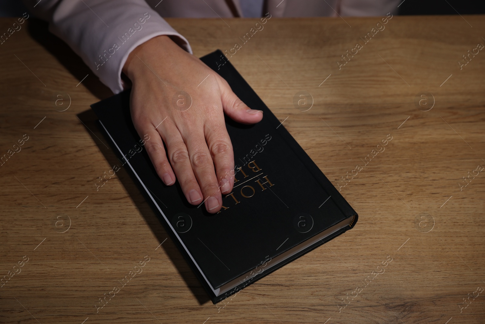 Photo of Woman taking oath with her hand on Bible at wooden table, above view