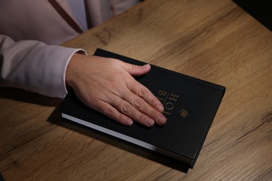 Photo of Woman taking oath with her hand on Bible at wooden table, above view