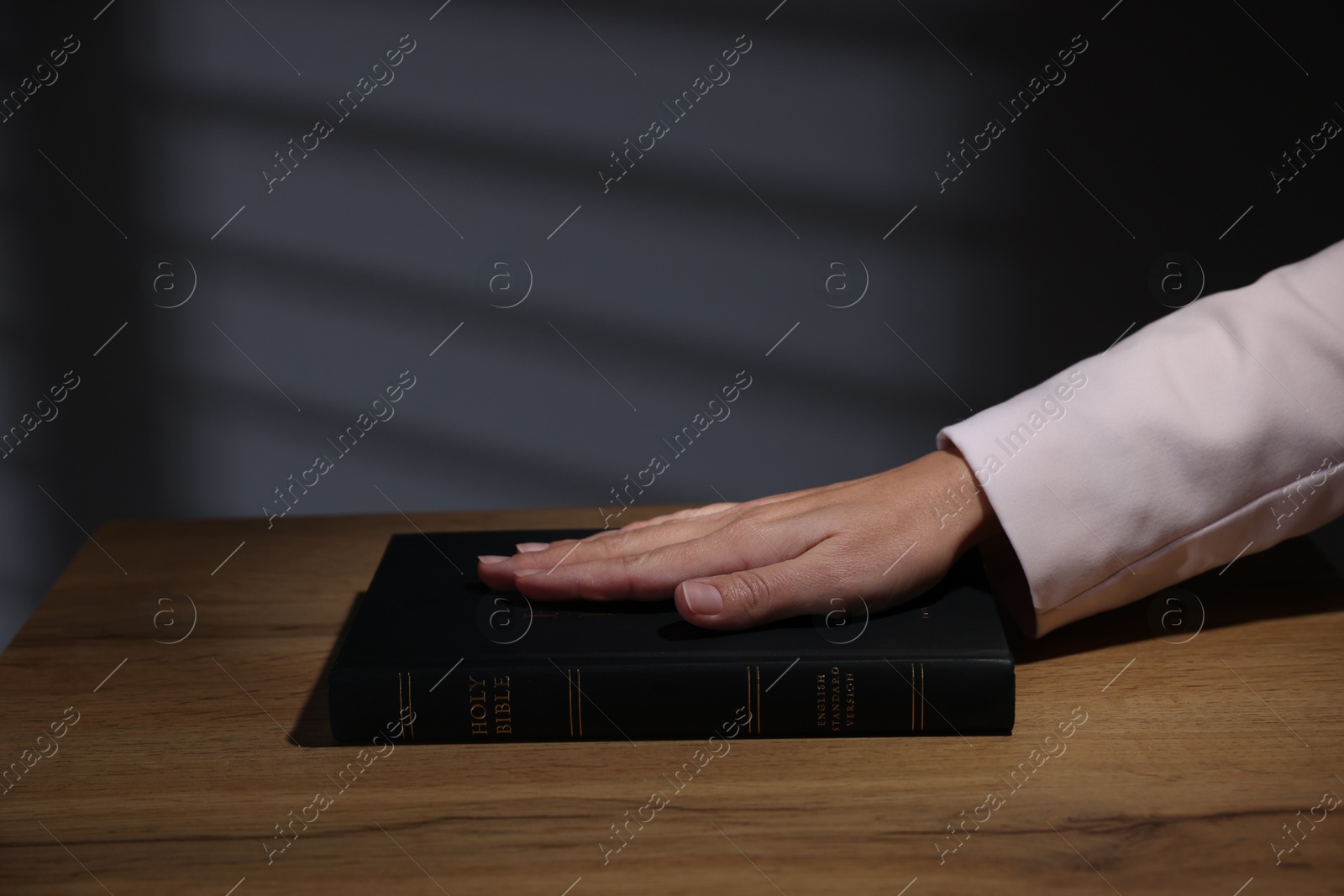 Photo of Woman taking oath with her hand on Bible at wooden table, closeup