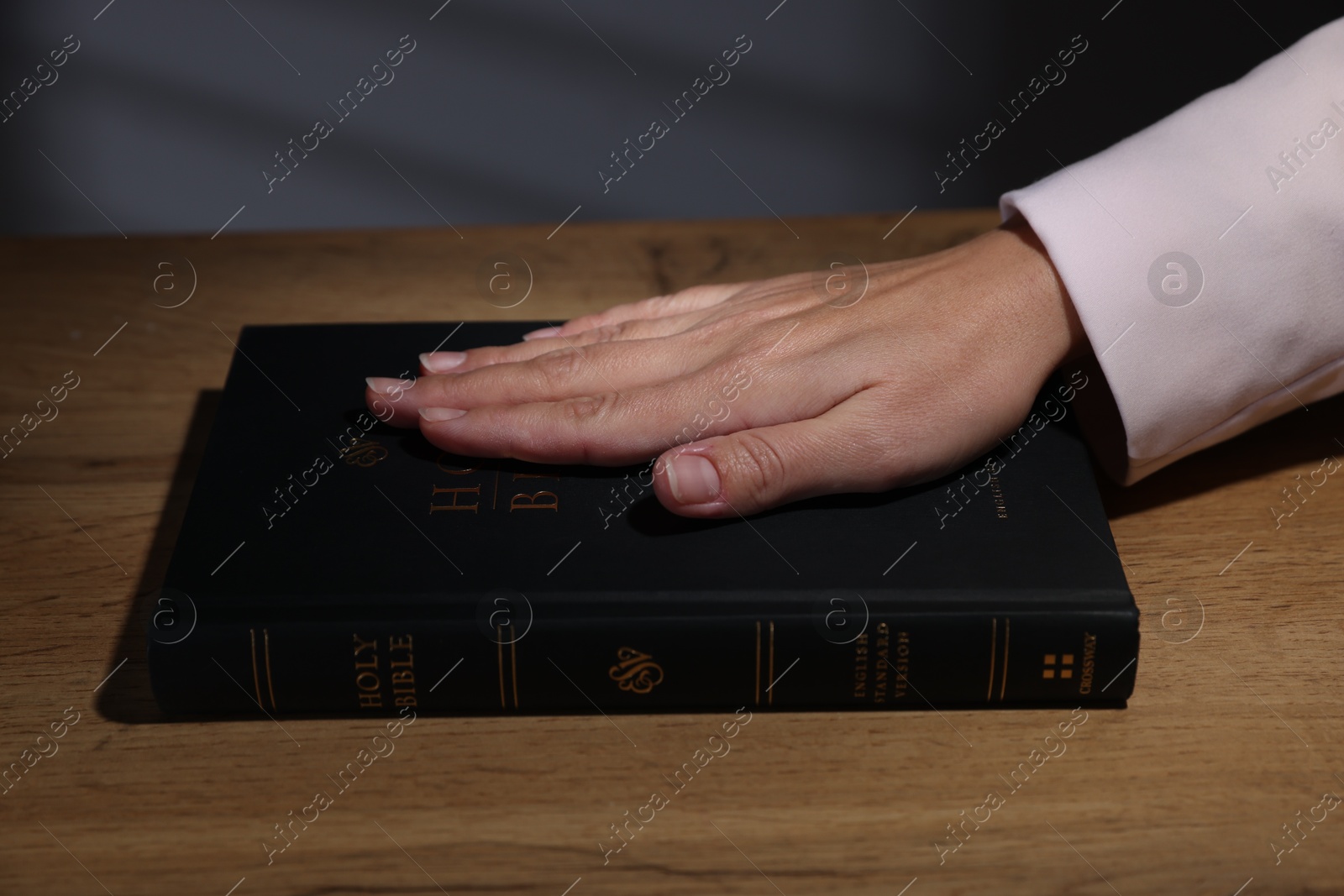 Photo of Woman taking oath with her hand on Bible at wooden table, closeup