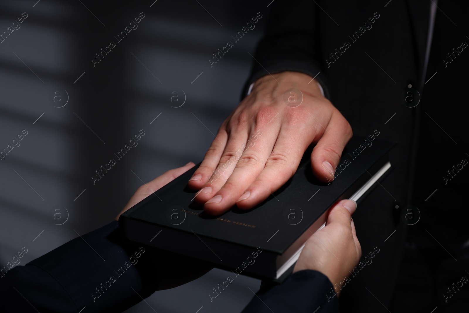 Photo of Man taking oath with his hand on Bible indoors, closeup