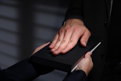 Photo of Man taking oath with his hand on Bible indoors, closeup