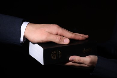 Photo of Man taking oath with his hand on Bible against black background, closeup