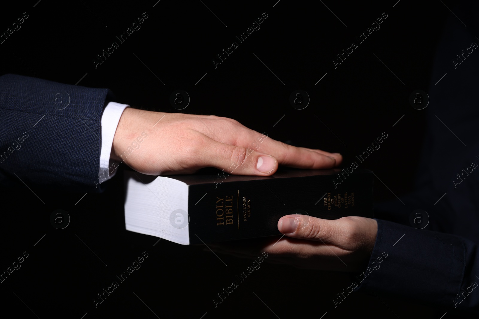 Photo of Man taking oath with his hand on Bible against black background, closeup