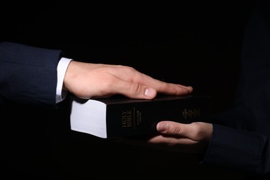 Photo of Man taking oath with his hand on Bible against black background, closeup