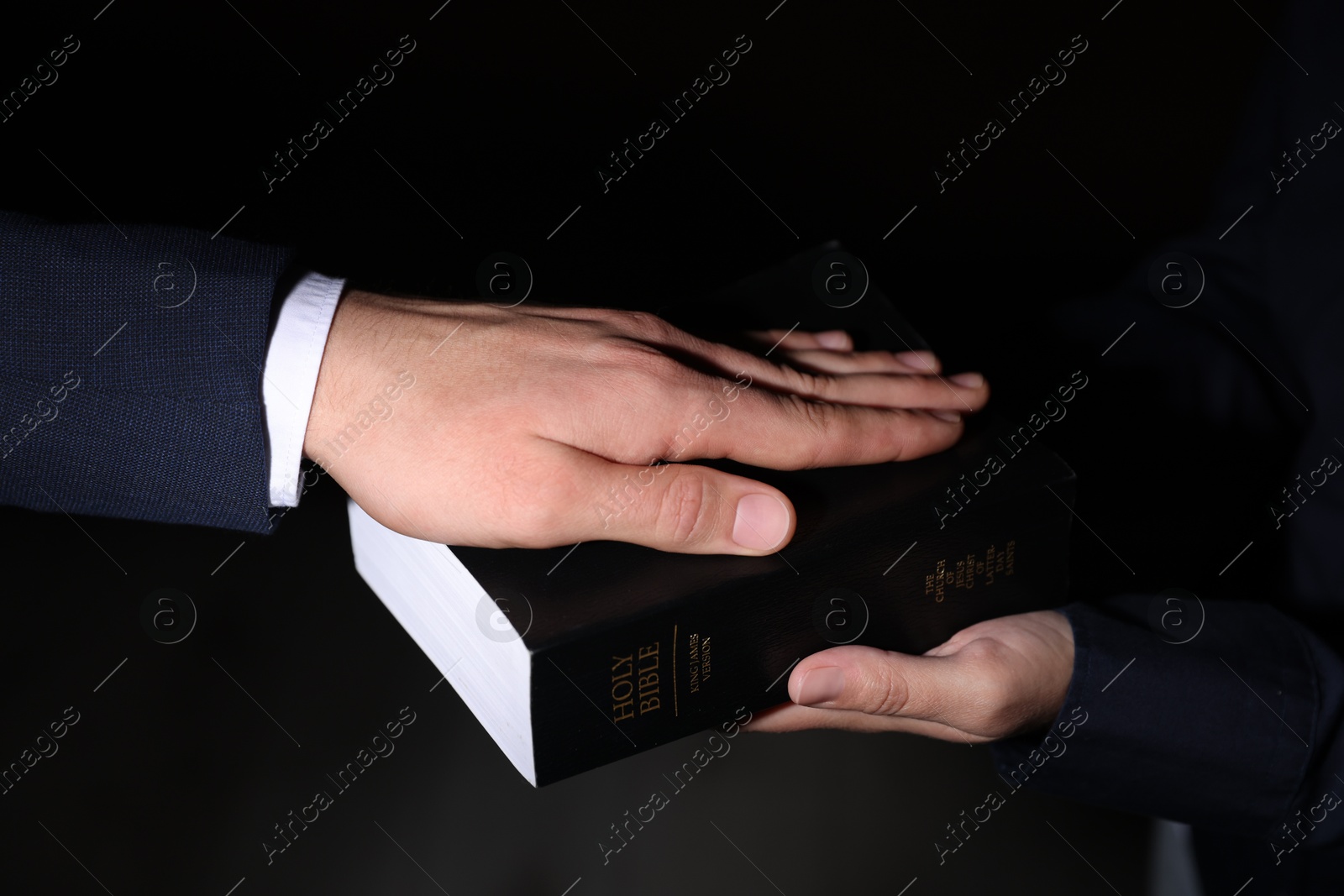 Photo of Man taking oath with his hand on Bible against black background, closeup