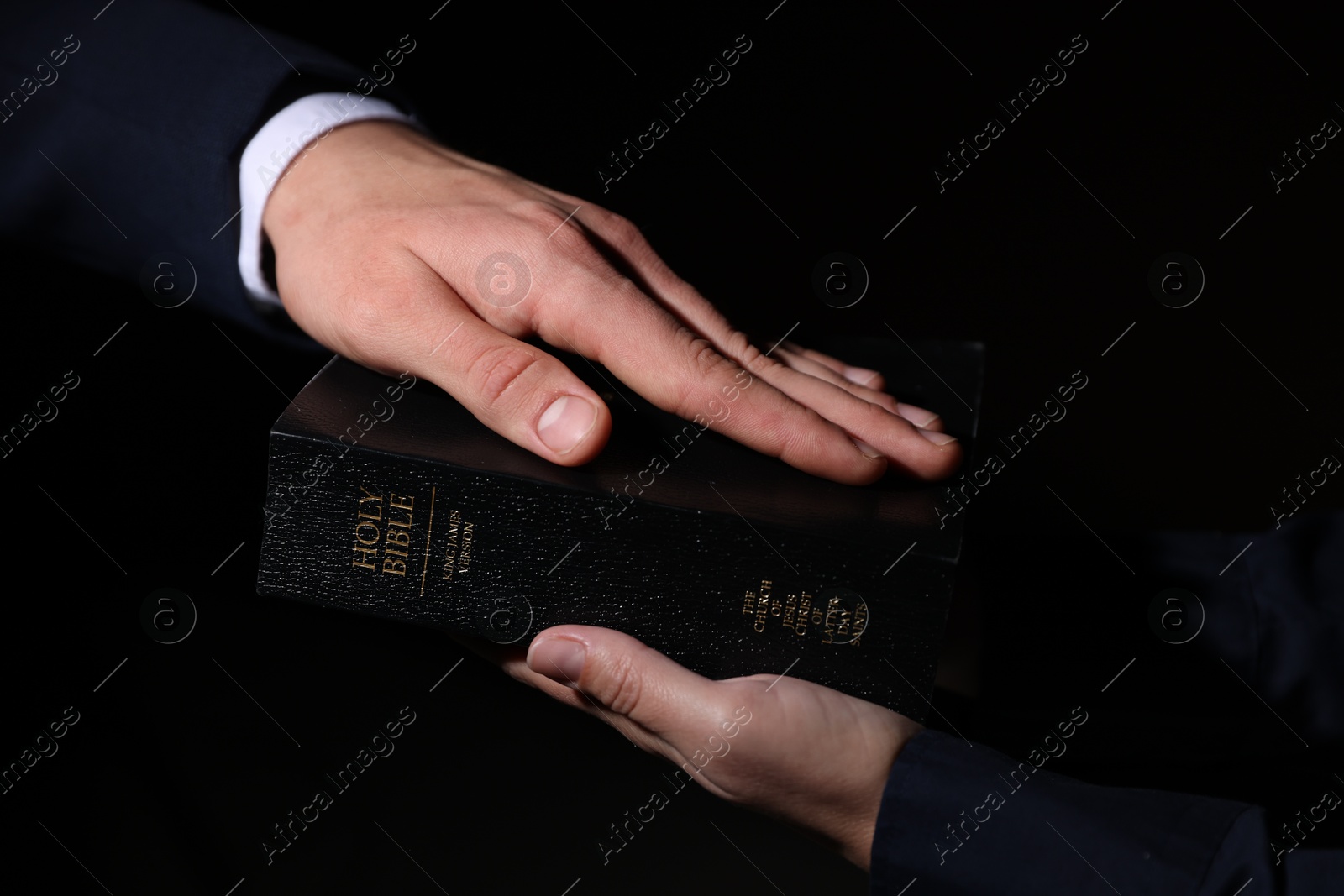 Photo of Man taking oath with his hand on Bible against black background, closeup