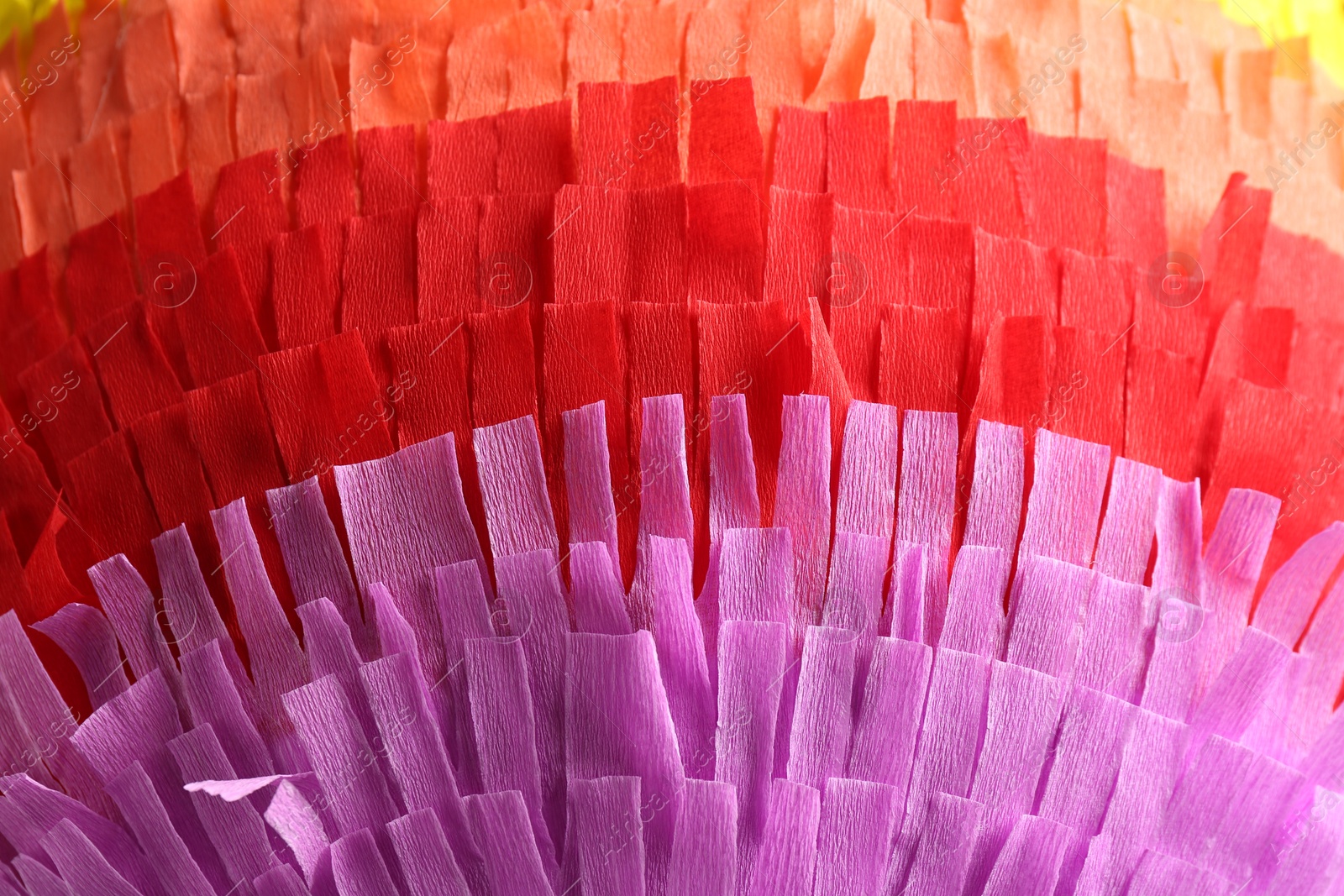 Photo of Pinata. Cut tissue paper in different colors as background, closeup