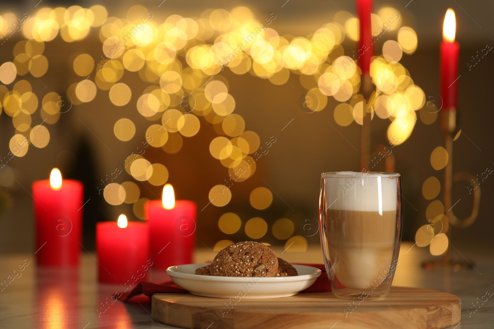 Photo of Aromatic coffee in glass, tasty cookies and burning candles on table against blurred Christmas lights. Bokeh effect