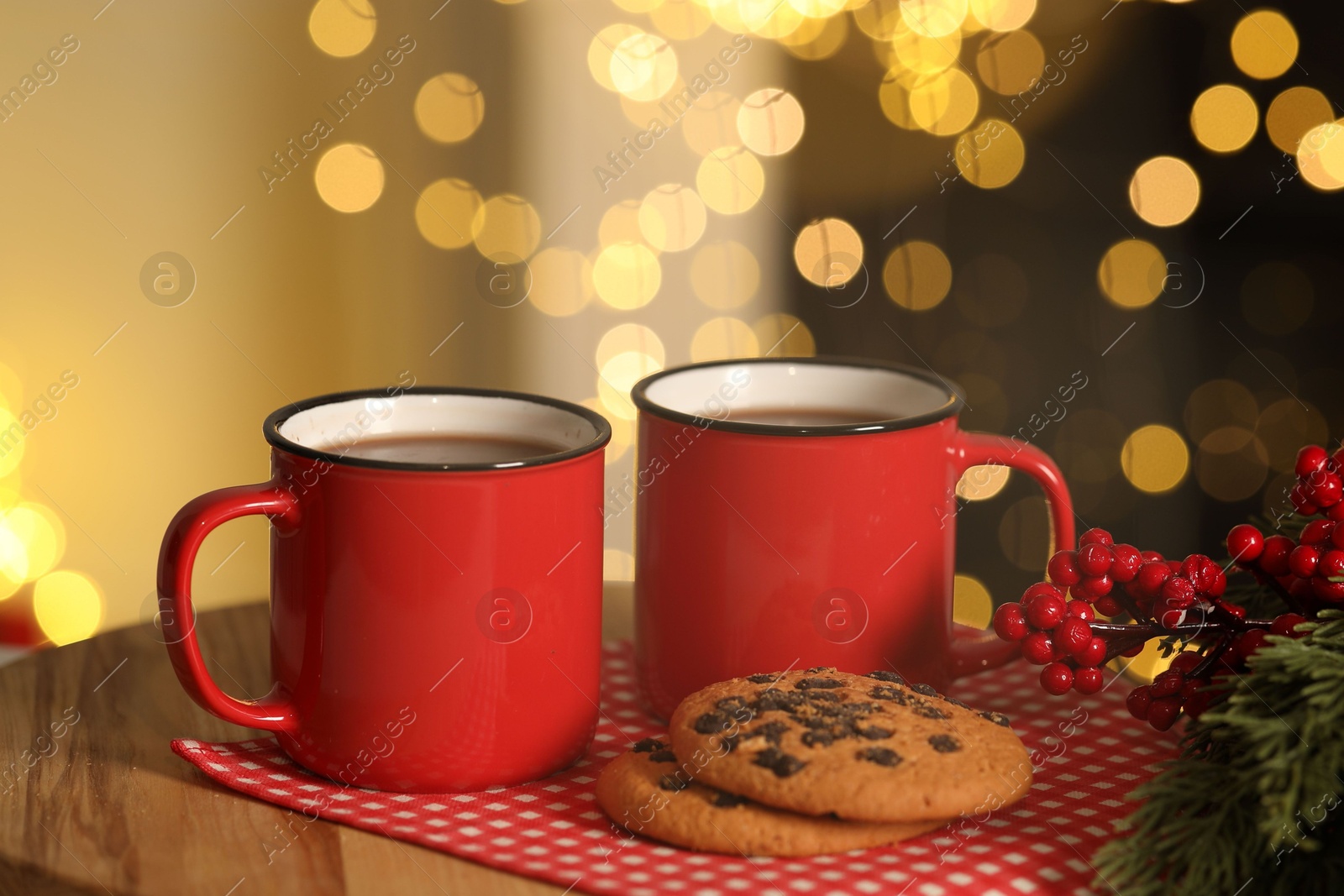 Photo of Tasty cocoa in cups, chocolate chip cookies and decorative branches on table against blurred Christmas lights. Bokeh effect