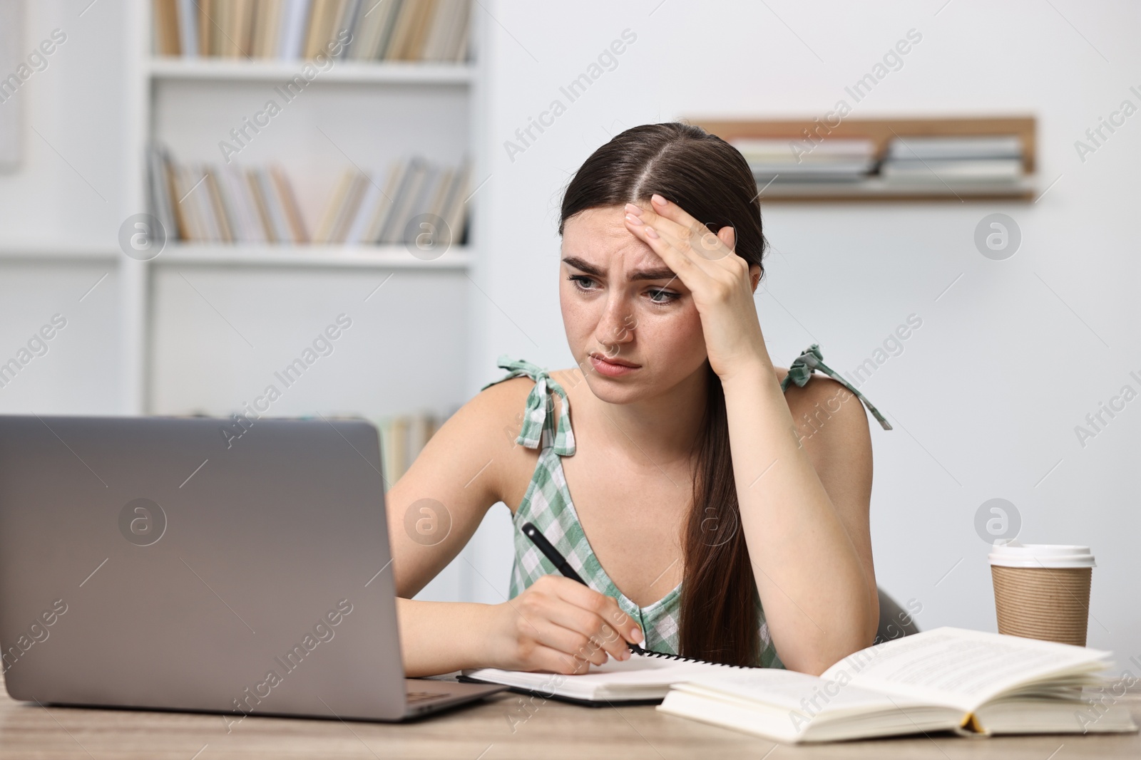 Photo of Tired student preparing for exam with laptop at table indoors