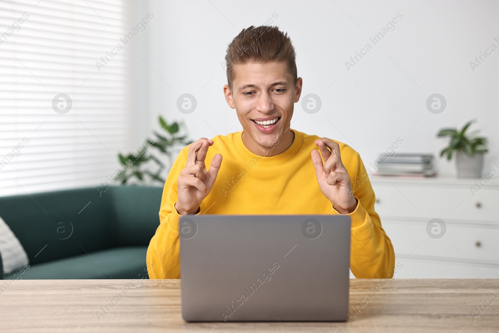 Photo of Student with crossed fingers at table with laptop indoors. Hope for good exam result