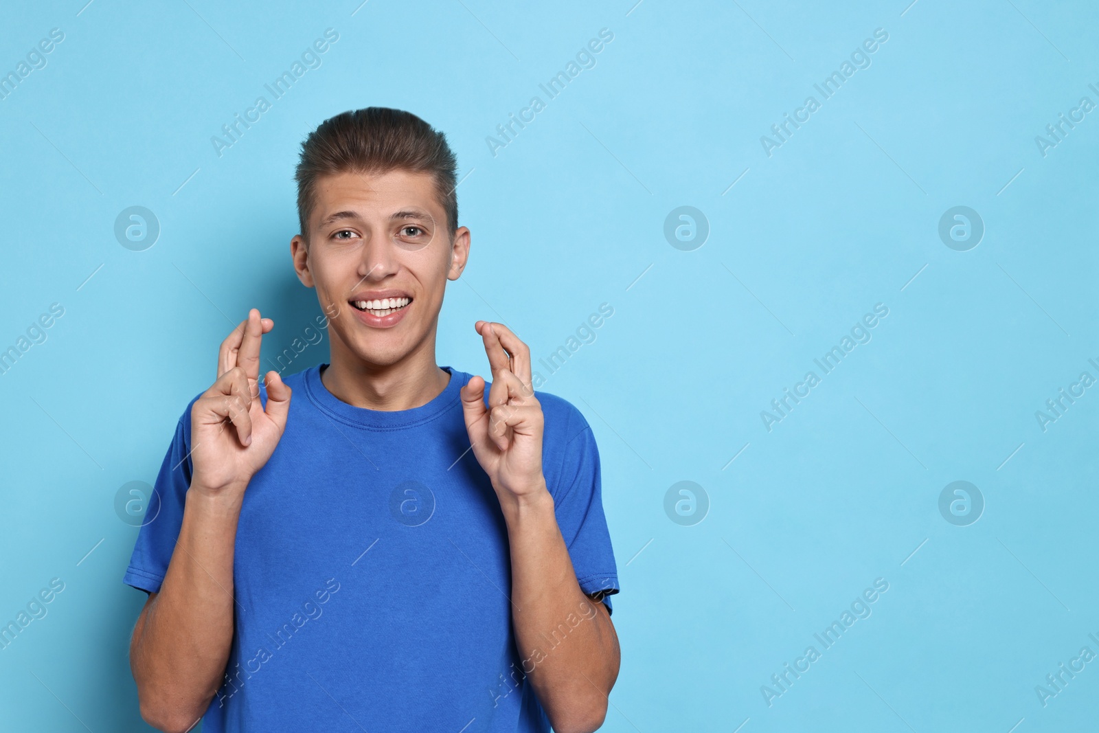 Photo of Student with crossed fingers on light blue background, space for text. Hope for good exam result