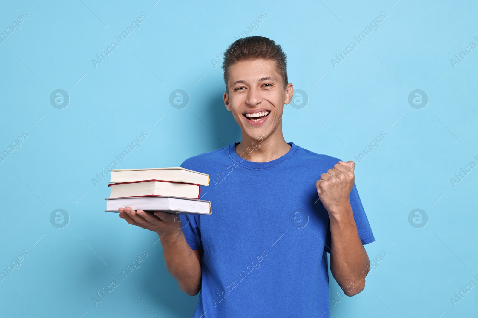 Photo of Happy student with stack of books on light blue background