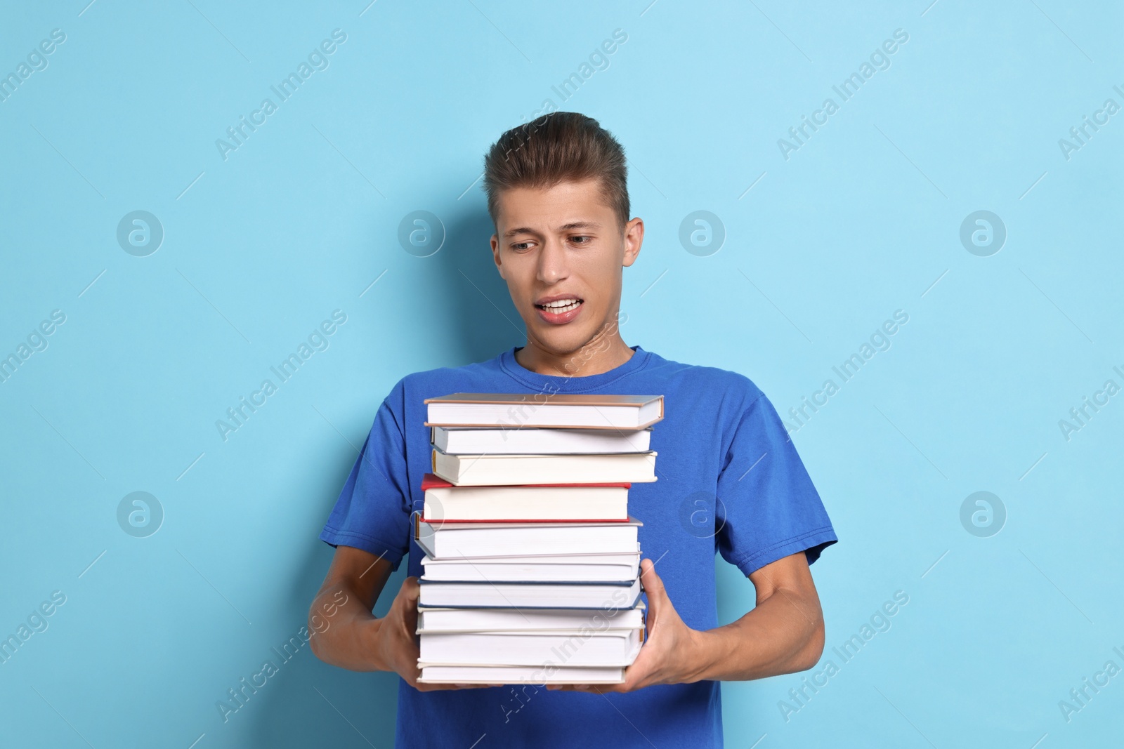 Photo of Emotional student with stack of books having stress before exam on light blue background