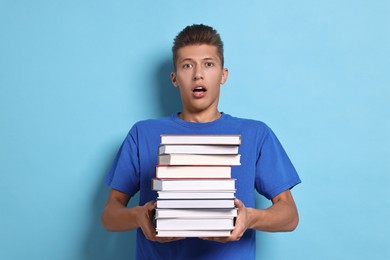 Emotional student with stack of books having stress before exam on light blue background