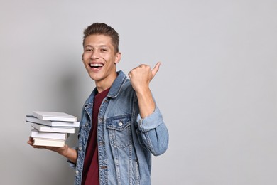 Photo of Happy student with stack of books showing thumbs up on grey background. Space for text