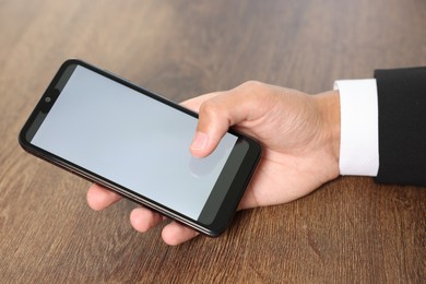 Photo of Man unlocking smartphone with fingerprint scanner at wooden table, closeup