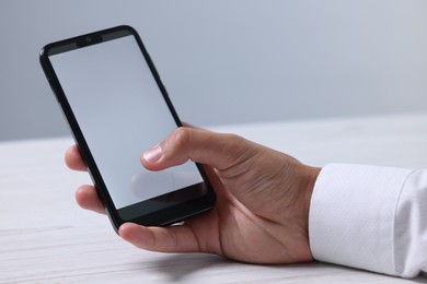 Photo of Man unlocking smartphone with fingerprint scanner at light wooden table, closeup