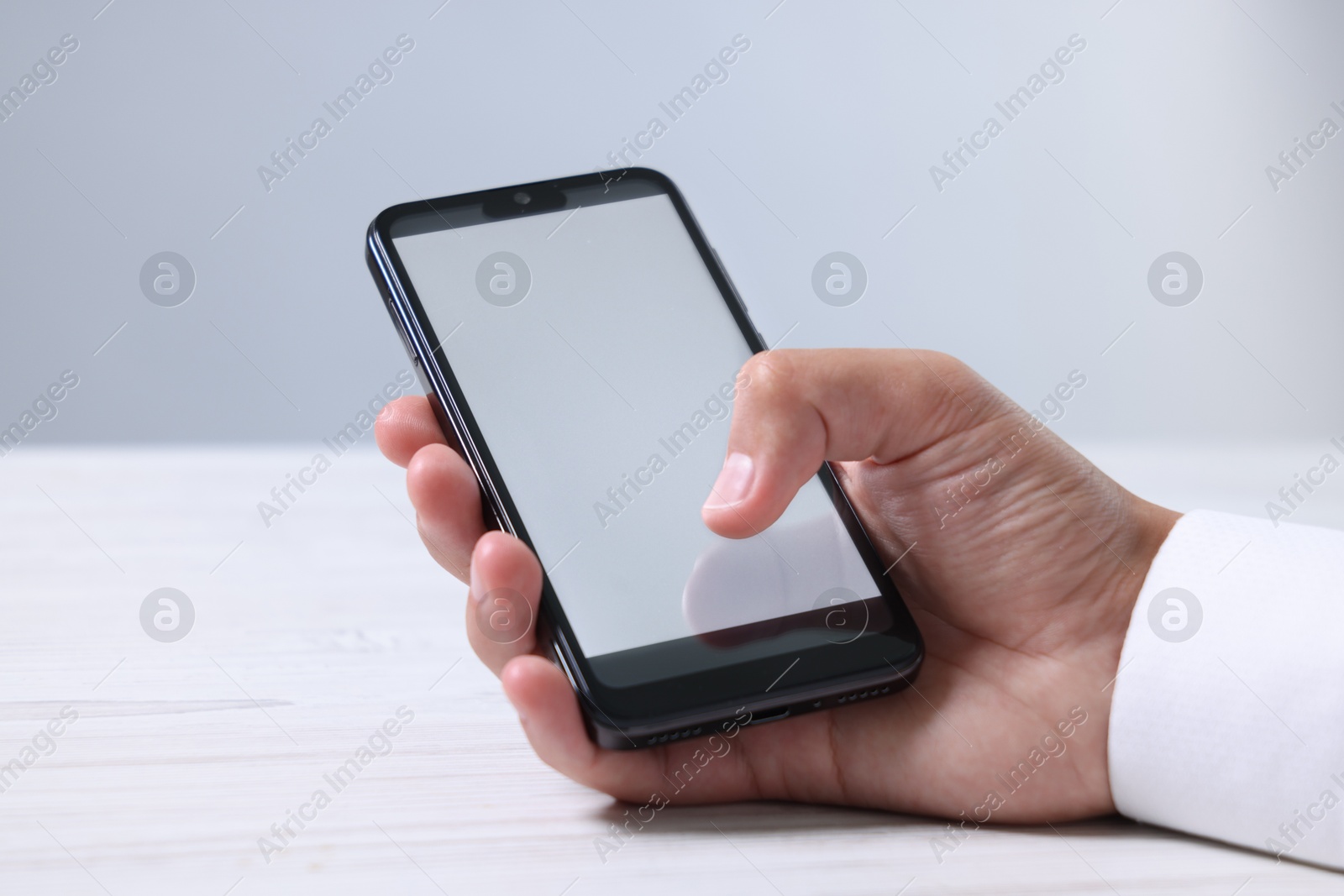 Photo of Man unlocking smartphone with fingerprint scanner at light wooden table, closeup