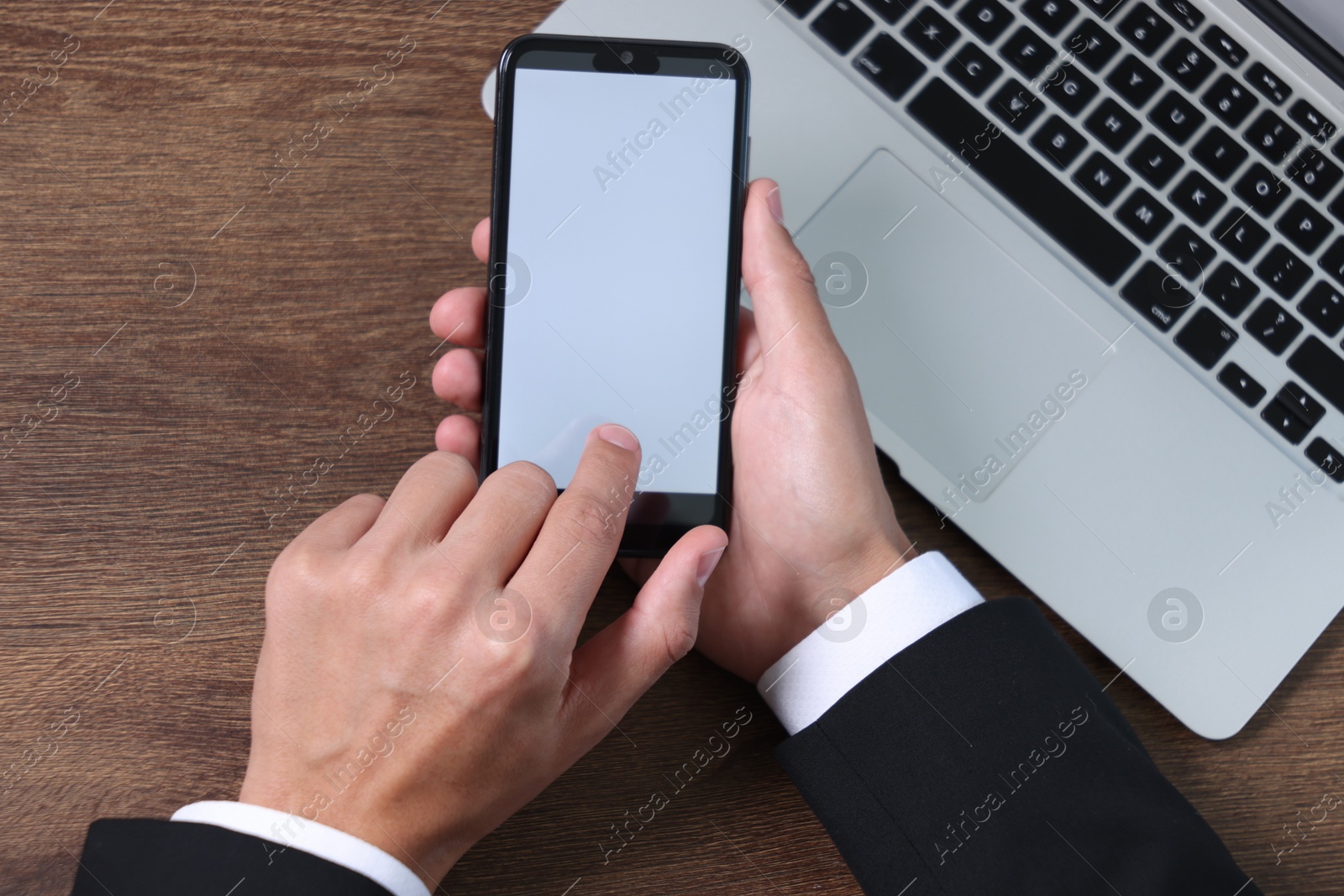 Photo of Man unlocking smartphone with fingerprint scanner near laptop at wooden table, top view