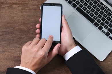 Photo of Man unlocking smartphone with fingerprint scanner near laptop at wooden table, top view