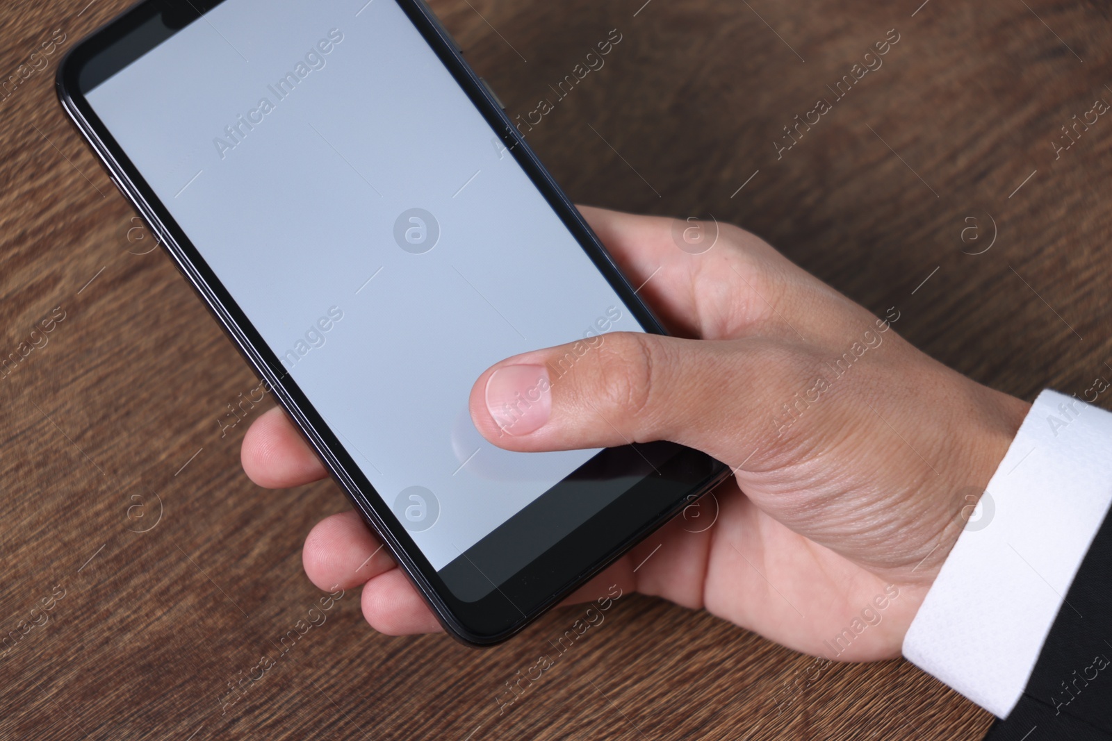 Photo of Man unlocking smartphone with fingerprint scanner at wooden table, closeup