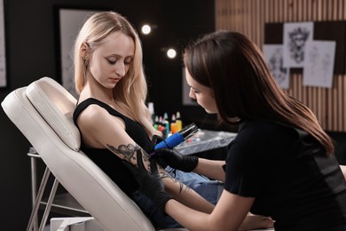 Photo of Professional artist tattooing woman with machine in salon