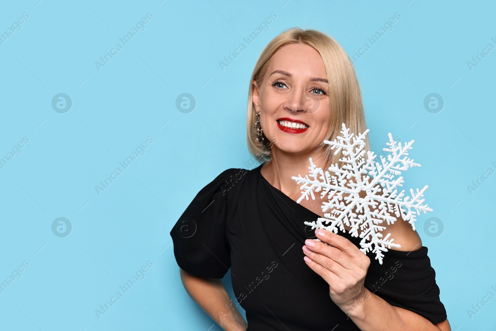 Photo of Smiling woman with decorative snowflake on light blue background, space for text. Christmas celebration